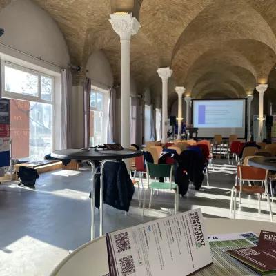 Bild zeigt Veranstaltungssaal mit leeren Stühlen und Leinwand